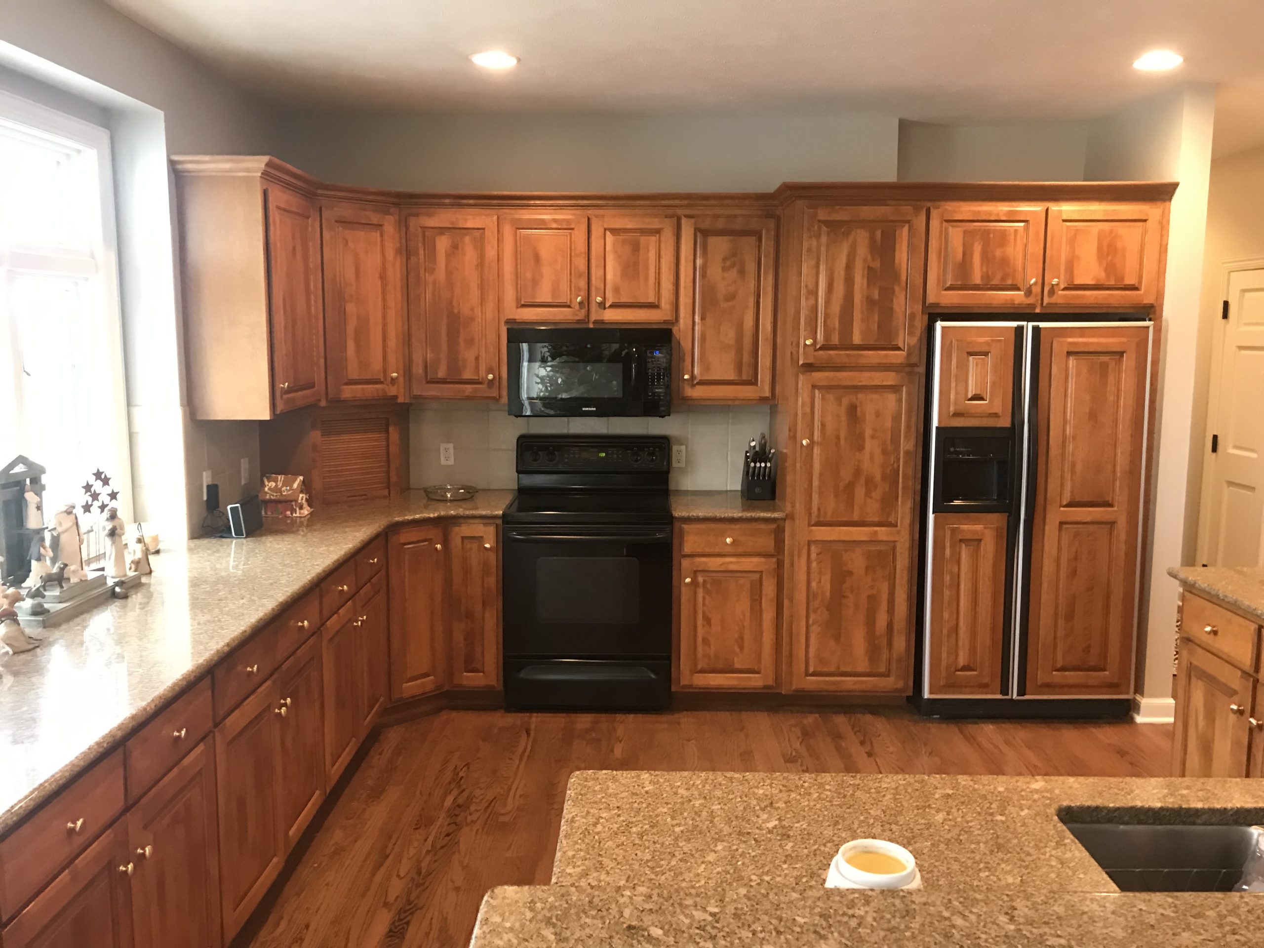 A kitchen with custom wooden cabinets, granite countertops, black appliances, and a double-door refrigerator. A small bowl is on the island in the foreground.